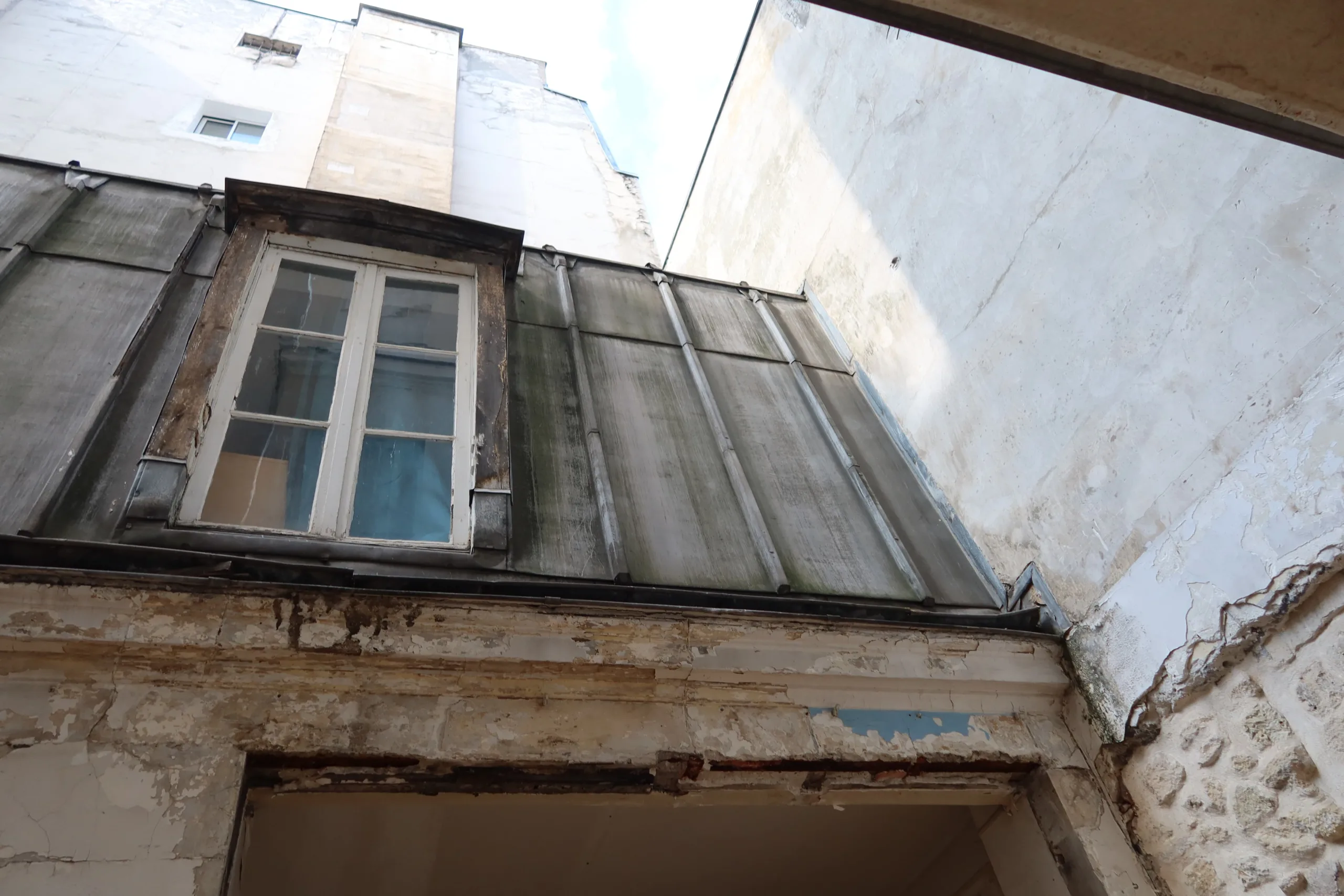 Cour intérieure d'un immeuble ancien avec façades dégradées et toiture en zinc marquée par l'humidité
